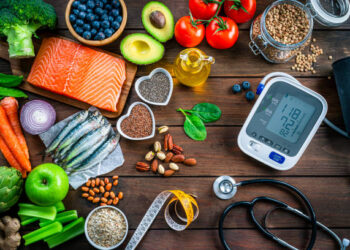 Healthy food for heart care: overhead view of healthy food rich in Omega-3 and antioxidants and a blood pressure monitor, tape measure and stethoscope shot on wooden table. The composition includes a salmon fillet, sardines, avocado, extra virgin olive oil, brown lentils, celery, artichoke blueberries, celery, carrots, brown lentils, asparagus, artichoke, broccoli, flax seeds, chia seeds and some nuts like almonds, pistachio and pecan. High resolution 42Mp studio digital capture taken with SONY A7rII and Zeiss Batis 40mm F2.0 CF lens