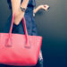 Fashionable beautiful big red handbag on the arm of the girl in a fashionable black dress, posing near the wall on a warm summer night. Warm color