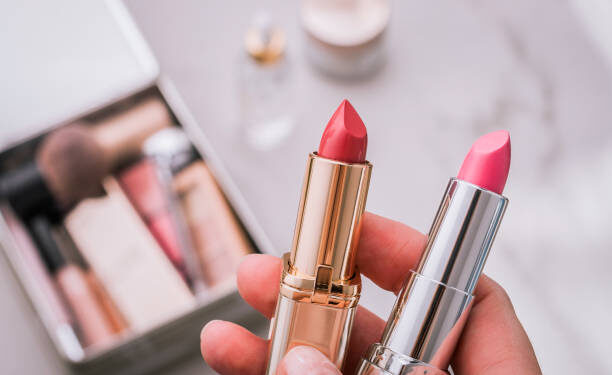 A person holds two lipsticks. Beauty products blurred background. Top view.