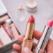 A person holds two lipsticks. Beauty products blurred background. Top view.