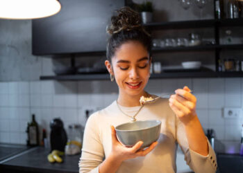 A young woman eats oatmeal in her kitchen, it is her healthy daily meal